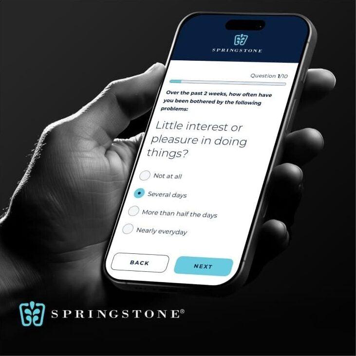 A black-and-white photo of a hand holding a smartphone displaying a mental health questionnaire, branded with the Springstone logo.